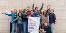 12 Personen stehen um das Plakat "Skills4Transformation" und winken fröhlich mit den Händen